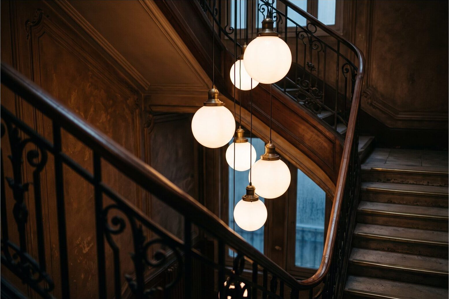 Suspension de cage d’escalier : cinq verres opalins échelonnés le long d’un câble noir, allumés dans la montée d’un immeuble ancien